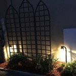 Small bed with decorative patio lights lit up at night, indian hawthorne planted.